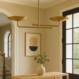 Modern brass linear chandelier with two dish-shaped shades hanging above a minimalist gray and white bedroom interior
Handmade brass pendant light fixture with dual disc shades in a modern bedroom with neutral décor
Luxury brushed brass two-arm linear chandelier installed above a bed in a contemporary minimalist room
Mid century modern brass ceiling light with two flat dome shades illuminating a cozy bedroom interior