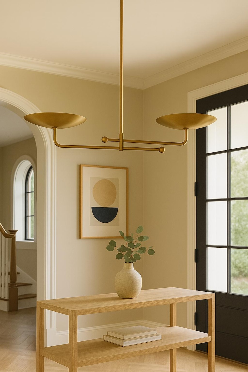 Modern brass linear chandelier with two dish-shaped shades hanging above a minimalist gray and white bedroom interior
Handmade brass pendant light fixture with dual disc shades in a modern bedroom with neutral décor
Luxury brushed brass two-arm linear chandelier installed above a bed in a contemporary minimalist room
Mid century modern brass ceiling light with two flat dome shades illuminating a cozy bedroom interior