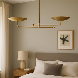 Modern brass linear chandelier with two dish-shaped shades hanging above a minimalist gray and white bedroom interior
Handmade brass pendant light fixture with dual disc shades in a modern bedroom with neutral décor
Luxury brushed brass two-arm linear chandelier installed above a bed in a contemporary minimalist room
Mid century modern brass ceiling light with two flat dome shades illuminating a cozy bedroom interior