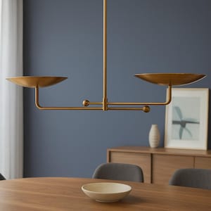 Modern brass linear chandelier with two dish-shaped shades hanging above a minimalist gray and white bedroom interior
Handmade brass pendant light fixture with dual disc shades in a modern bedroom with neutral décor
Luxury brushed brass two-arm linear chandelier installed above a bed in a contemporary minimalist room
Mid century modern brass ceiling light with two flat dome shades illuminating a cozy bedroom interior