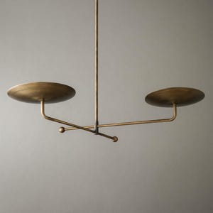 Modern brass linear chandelier with two dish-shaped shades hanging above a minimalist gray and white bedroom interior
Handmade brass pendant light fixture with dual disc shades in a modern bedroom with neutral décor
Luxury brushed brass two-arm linear chandelier installed above a bed in a contemporary minimalist room
Mid century modern brass ceiling light with two flat dome shades illuminating a cozy bedroom interior