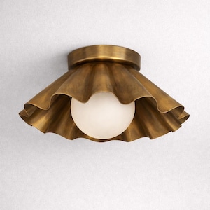 May include: A brass-colored ceiling light fixture with a ruffled shade and a spherical, frosted glass bulb. The fixture has a circular base and a decorative, wavy edge on the shade. The overall design is vintage-inspired.