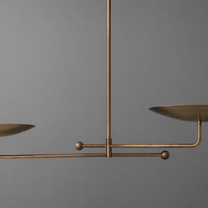 Modern brass linear chandelier with two dish-shaped shades hanging above a minimalist gray and white bedroom interior
Handmade brass pendant light fixture with dual disc shades in a modern bedroom with neutral décor
Luxury brushed brass two-arm linear chandelier installed above a bed in a contemporary minimalist room
Mid century modern brass ceiling light with two flat dome shades illuminating a cozy bedroom interior