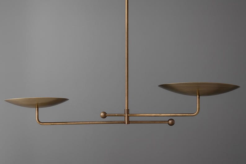 Modern brass linear chandelier with two dish-shaped shades hanging above a minimalist gray and white bedroom interior
Handmade brass pendant light fixture with dual disc shades in a modern bedroom with neutral décor
Luxury brushed brass two-arm linear chandelier installed above a bed in a contemporary minimalist room
Mid century modern brass ceiling light with two flat dome shades illuminating a cozy bedroom interior