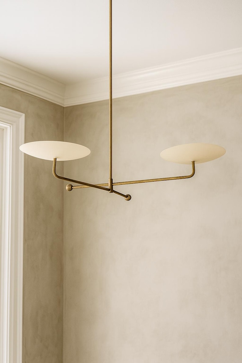 Modern brass linear chandelier with two dish-shaped shades hanging above a minimalist gray and white bedroom interior
Handmade brass pendant light fixture with dual disc shades in a modern bedroom with neutral décor
Luxury brushed brass two-arm linear chandelier installed above a bed in a contemporary minimalist room
Mid century modern brass ceiling light with two flat dome shades illuminating a cozy bedroom interior