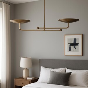 Modern brass linear chandelier with two dish-shaped shades hanging above a minimalist gray and white bedroom interior
Handmade brass pendant light fixture with dual disc shades in a modern bedroom with neutral décor
Luxury brushed brass two-arm linear chandelier installed above a bed in a contemporary minimalist room
Mid century modern brass ceiling light with two flat dome shades illuminating a cozy bedroom interior