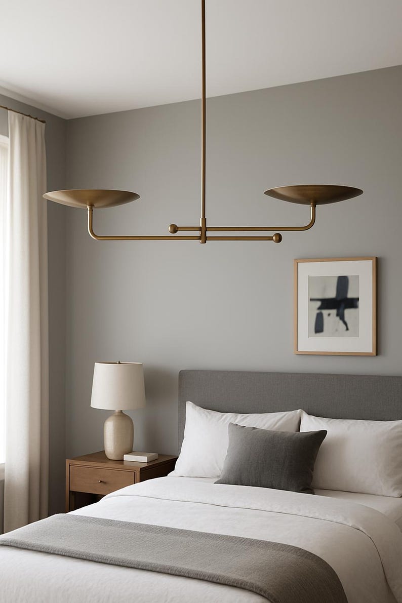 Modern brass linear chandelier with two dish-shaped shades hanging above a minimalist gray and white bedroom interior
Handmade brass pendant light fixture with dual disc shades in a modern bedroom with neutral décor
Luxury brushed brass two-arm linear chandelier installed above a bed in a contemporary minimalist room
Mid century modern brass ceiling light with two flat dome shades illuminating a cozy bedroom interior
