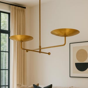 Modern brass linear chandelier with two dish-shaped shades hanging above a minimalist gray and white bedroom interior
Handmade brass pendant light fixture with dual disc shades in a modern bedroom with neutral décor
Luxury brushed brass two-arm linear chandelier installed above a bed in a contemporary minimalist room
Mid century modern brass ceiling light with two flat dome shades illuminating a cozy bedroom interior