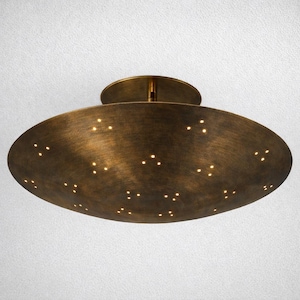 May include: A bronze-colored, oval-shaped ceiling light fixture. The fixture has a series of small, evenly spaced holes that emit light. The light has a circular base and a stem that connects to the ceiling.
