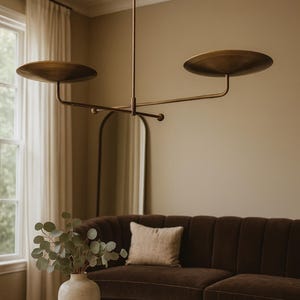 Modern brass linear chandelier with two dish-shaped shades hanging above a minimalist gray and white bedroom interior
Handmade brass pendant light fixture with dual disc shades in a modern bedroom with neutral décor
Luxury brushed brass two-arm linear chandelier installed above a bed in a contemporary minimalist room
Mid century modern brass ceiling light with two flat dome shades illuminating a cozy bedroom interior