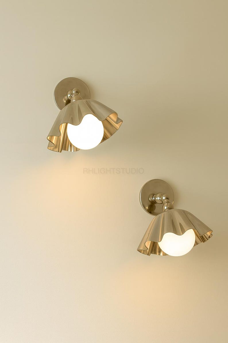 K&ouml;nnte beinhalten: Zwei Wandleuchten mit Messing-Finish, jede mit einem ger&uuml;schten Schirm und einer kugelf&ouml;rmigen, leuchtenden Lichtquelle. Die Leuchten sind an einer neutralfarbenen Wand montiert. Der Text "RHLIGHTSTUDIO" ist sichtbar.