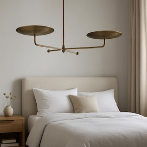 Modern brass linear chandelier with two dish-shaped shades hanging above a minimalist gray and white bedroom interior
Handmade brass pendant light fixture with dual disc shades in a modern bedroom with neutral décor
Luxury brushed brass two-arm linear chandelier installed above a bed in a contemporary minimalist room
Mid century modern brass ceiling light with two flat dome shades illuminating a cozy bedroom interior