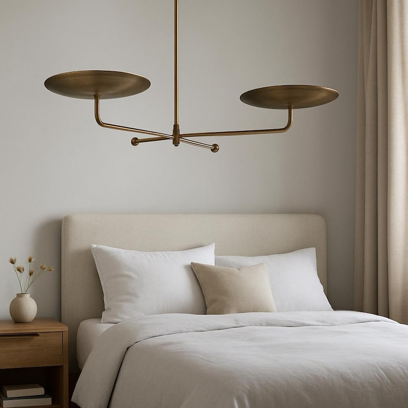 Modern brass linear chandelier with two dish-shaped shades hanging above a minimalist gray and white bedroom interior
Handmade brass pendant light fixture with dual disc shades in a modern bedroom with neutral décor
Luxury brushed brass two-arm linear chandelier installed above a bed in a contemporary minimalist room
Mid century modern brass ceiling light with two flat dome shades illuminating a cozy bedroom interior
