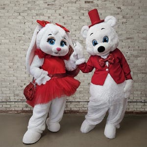Peut inclure: Deux costumes de mascottes : un lapin blanc avec une robe rouge, un nœud et un sac à main, et un ours blanc avec une veste rouge et un haut-de-forme. Les deux ont les yeux bleus et se tiennent la main. Fond de mur en briques.