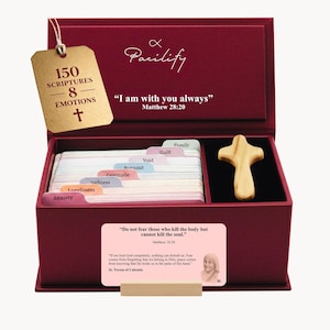 Peut inclure: Un coffret bordeaux avec une croix en bois et un jeu de cartes. Le couvercle de la boîte porte le texte "Pacilify" et un verset biblique. Les cartes sont étiquetées avec des émotions comme "Anxiété" et "Solitude". Une étiquette indique "150 Écritures - 8 Émotions".