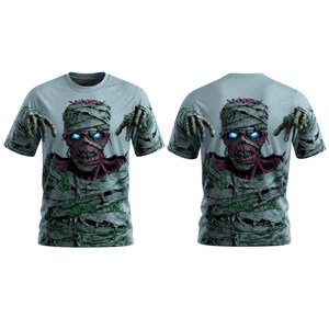 Puede incluir: Una camiseta de manga corta de color azul claro con un estampado gráfico de una momia con ojos azules brillantes, dientes expuestos y envuelta en vendas andrajosas. El diseño muestra las manos de la momia extendidas con texturas verde musgo.