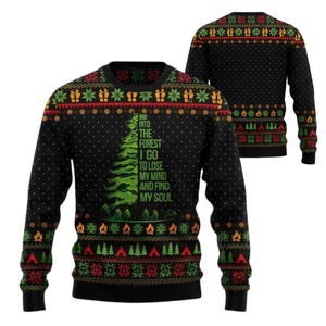Könnte beinhalten: Ein schwarzer Langarmpullover mit einer grünen Tannenbaumgrafik und dem Text "AND INTO THE FOREST I GO TO LOSE MY MIND AND FIND MY SOUL." Das Kleidungsstück zeigt ein wiederkehrendes Muster aus roten, grünen und gelben Lagerfeuern, Zelten und Schneeflocken.