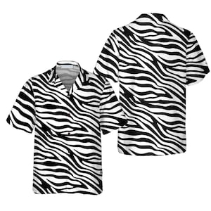 Puede incluir: Dos camisas de manga corta con botones y un estampado de rayas de cebra en blanco y negro. Las camisas tienen cuello y un corte holgado. El estampado de cebra cubre toda la camisa, incluidas las mangas y la espalda.