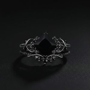 May include: Black ring set featuring a square-cut black gemstone as the centerpiece. The ring is accented with smaller black stones and decorative filigree. The set includes a matching band, creating a cohesive and elegant look.