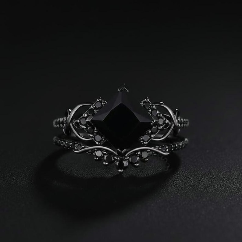 May include: Black ring set featuring a square-cut black gemstone as the centerpiece. The ring is accented with smaller black stones and decorative filigree. The set includes a matching band, creating a cohesive and elegant look.