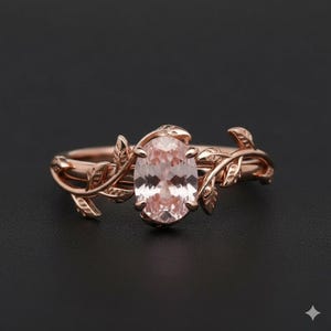 May include: Rose gold ring featuring an oval, light pink gemstone. The ring's band is adorned with delicate leaf and vine detailing, creating a nature-inspired design. The ring is set against a dark background.