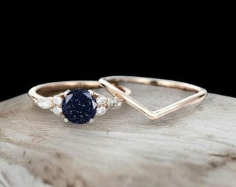 May include: Two rose gold rings. One ring features a large, dark blue gemstone with a speckled appearance, surrounded by smaller white stones. The second ring is a simple V-shaped band.