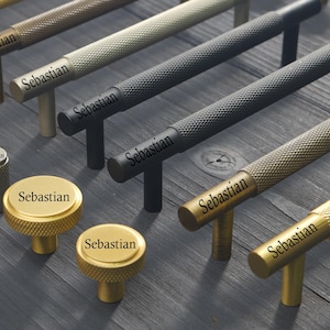 May include: A collection of metal cabinet hardware including long bar pulls and round knobs with a textured knurled surface. The hardware comes in various metallic finishes such as gold, silver, and matte black, each featuring the text Sebastian.