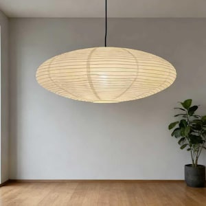 以下が含まれることがあります： クリーム色の紙シェードと黒い水平線が入った楕円形のペンダントライト。黒いコードで吊り下げられており、薄い灰色の壁と木の床がある部屋にあります。鉢植えの植物が隅にあります。スタイリッシュなインテリアデザイン要素です。