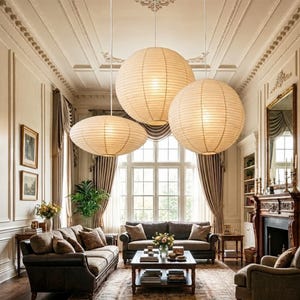 May include: Three spherical pendant lights made of off-white paper with visible horizontal ribbing, suspended from the ceiling at varying heights. The lights feature a warm, glowing illumination and are arranged in a cluster above a living room.