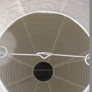 以下が含まれることがあります： 円形の白い紙提灯。白い金属フレームと中央に暗い開口部があります。プリーツ加工された紙がストライプ模様を作り出しています。屋内または屋外での使用に適した装飾品です。