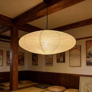 以下が含まれることがあります： 木製の梁と伝統的な日本の美術品がある部屋の天井から、大きな楕円形の紙のランタンが吊り下げられています。 ランタンはクリーム色で水平線があり、温かい光を放っています。 部屋はミニマリストなデザインです。