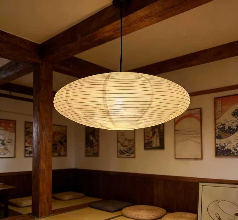 以下が含まれることがあります： 木製の梁と伝統的な日本の美術品がある部屋の天井から、大きな楕円形の紙のランタンが吊り下げられています。 ランタンはクリーム色で水平線があり、温かい光を放っています。 部屋はミニマリストなデザインです。