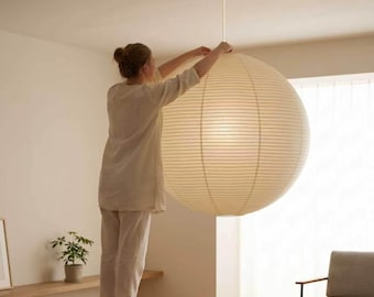 May include: A large, spherical paper pendant light fixture with a ribbed texture, suspended from the ceiling by a thin white cord. The lamp features a warm, off-white color and a rounded shape, providing a soft, diffused light throughout the room.