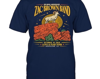 Puede incluir: Una camiseta azul marino de manga corta con un gráfico de un carnero de las Rocosas sobre una formación rocosa roja. El texto dice: RED ROCKS AMPHITHEATRE ZAC BROWN BAND OCTOBER 19, 2026 LOVE & FEAR TOUR MORRISON, CO. Incluye una luna amarilla y estrellas.