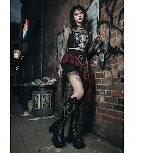 May include: A black crop top with a white graphic print, layered under a black fishnet long-sleeve shirt. The outfit includes a red and black plaid skirt with an attached black lace hem, a silver chain detail, and black platform boots with buckles.