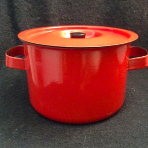 May include: A red enamel cooking pot with a matching lid. The pot has two side handles and a black knob on the lid. The pot is a vibrant red color and appears to be made of metal.