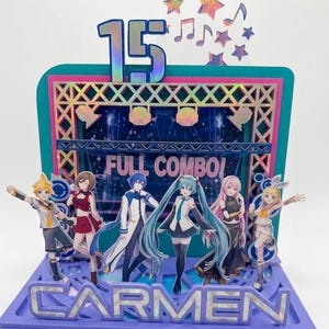 Puede incluir: Un adorno para tarta de papel multicapa con seis personajes de estilo anime frente a un escenario. El diseño incluye el número 15, notas musicales, estrellas y el texto FULL COMBO y CARMEN con un acabado holográfico sobre una base morada.