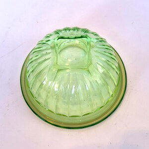 May include: A vintage, light green glass bowl with a ribbed exterior design. The bowl has a circular base and a square, raised center. The rim and base have a slightly darker green hue.