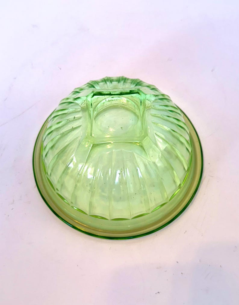 May include: A vintage, light green glass bowl with a ribbed exterior design. The bowl has a circular base and a square, raised center. The rim and base have a slightly darker green hue.
