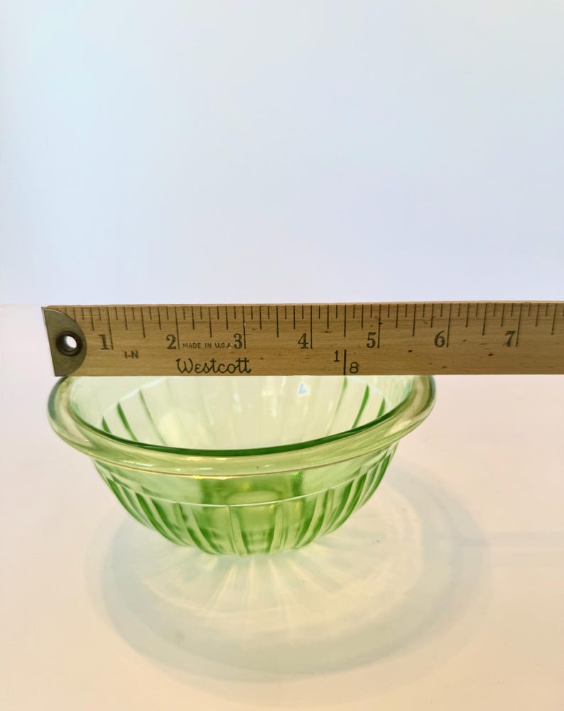 May include: A small, light green glass bowl with vertical ribbed detailing. The bowl is approximately 5 inches in diameter. A wooden ruler is placed across the top of the bowl. The text "MADE IN U.S.A." and "Westcott" are visible on the ruler.