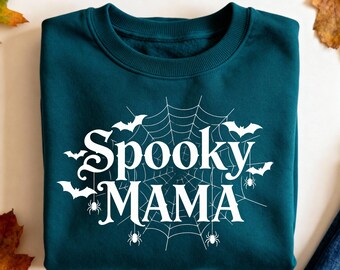 May include: A teal sweatshirt with the words "Spooky MAMA" in white, surrounded by a spiderweb design, bats, and spiders. This Halloween-themed sweatshirt is perfect for the spooky season.