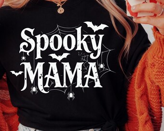 May include: Black t-shirt with the words "Spooky Mama" in white, featuring bats, spiderwebs, and spiders. The shirt is a Halloween-themed design, perfect for the spooky season.