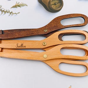 Puede incluir: Tres pinzas de servir de madera. Una es de color marrón oscuro y dos son de color marrón claro. La pinza del medio tiene grabado el nombre "Sallen". Cada pinza tiene un diseño similar a unas tijeras con un mango y un extremo de agarre, conectados por un tornillo color latón.