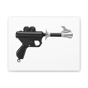 May include: A black and silver ray gun, likely a prop or toy, against a white background. The gun features a trigger, handle, and two circular elements on top. The barrel has a silver tip.