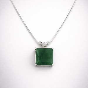 Op de afbeelding: Een zilveren ketting met een vierkante, smaragdgroene hanger. De hanger is gezet in een zilveren montuur en heeft een kleine, ronde diamant accent. De ketting hangt aan een fijne zilveren ketting.