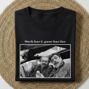 Könnte beinhalten: Schwarzes Sweatshirt mit Rundhalsausschnitt und dem Text "Work hard, pour harder." Unter dem Text befindet sich ein Schwarz-Weiß-Bild von zwei Männern in einem Auto. Ein Mann hält eine Bierdose.