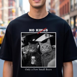 Könnte beinhalten: Schwarzes T-Shirt mit einer Grafik von zwei Katzen in einem Auto, eine hält ein Bier und eine Zigarette. Der Text "NO KINGS" ist durchgestrichen, darunter steht "Only a Few Small Beers".