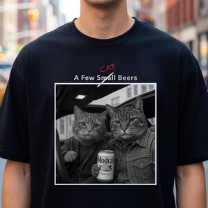 May include: Black t-shirt with a graphic of two cats in a car, one holding a can of "Modcat" beer. The text "CAT A Few Small Beers" is above the graphic in red and white.