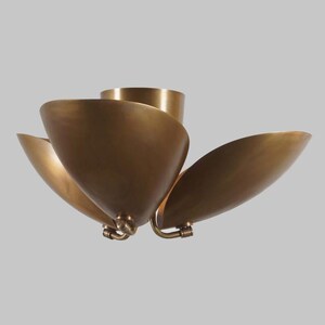 May include: A brass-colored ceiling light fixture with a floral design. The fixture has four curved, petal-shaped shades that extend outward from a central cylindrical base. The shades are a warm, metallic color, and the fixture is mounted on a neutral background.