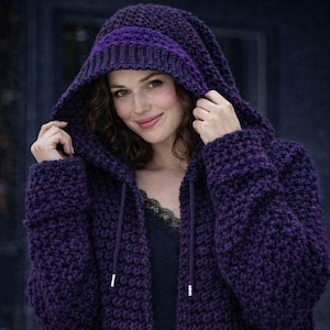 May include: A deep purple, hooded sweater with a textured knit design. The hood is lined with a darker purple band. The sweater has a drawstring closure and is worn by a person.